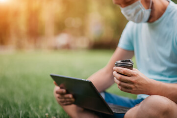 A quarantined man works remotely on a laptop. Remote work of a freelancer in a park in a mask. Relations with technology in Covid 2019.virtual: happy hour, party, graduation, coffee, date, dinner part