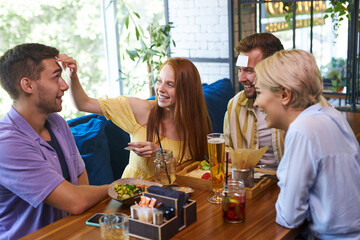 young people have funny game in cafe, best friends have happy holiday, sit with stickers on forehead, develop imagination