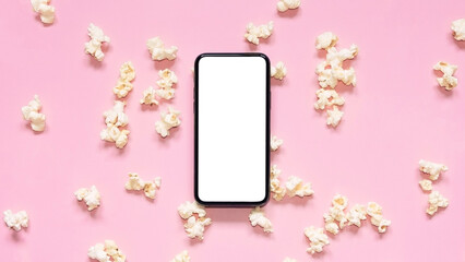 Flat lay scattered popcorn with mobile phone with blank screen on pink background. Mockup phone with white copy space. Smartphone application for online cinema, films and media on a mobile device.