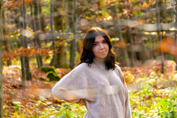 Portrait of a young pretty brunette wearing a beige sweater through two branches in a colorful autumn forest in October in Bavaria, Germany