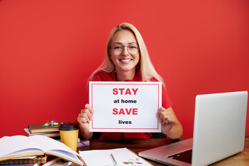 pretty caucasian blonde female ask people stay home, work at home, hold tablet in hands and look at camera isolated over red background