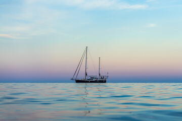 Fototapeta premium Calm. Nice weather at sunset, calm sea or ocean. There are few clouds and can be seen very far. A boat with lowered sails sails in the distance.