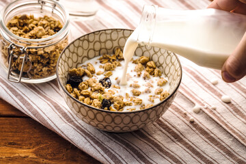 Breakfast food background. Milk Pouring Over Granola  on light table napkin,  Healthy vegetarian breakfast. Diet Nutrition Concept