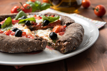 Pizza nera ai sette cereali con mozzarella, pomodorini, olive e basilico, Cucina Italiana
