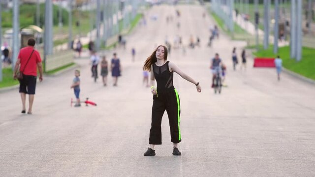girl dancing on the street. Blurry silhouettes of people are visible in the background. Hip hop. Contemporary choreography. Summer evening. Sunny sunset. Slow motion
