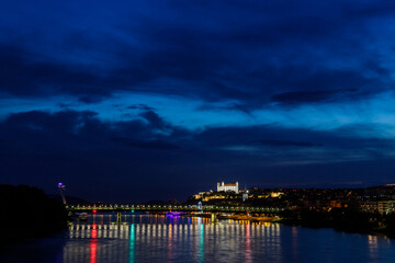 Fototapeta na wymiar Night over Danube river with lightened castle and SNP bridge, known landmarks in Bratislava, capital of Slovakia. Reflection of lights in water surface.