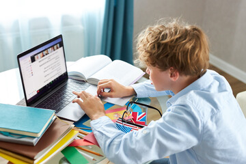 Fototapeta premium teen schoolboy prepares a presentation, writes a report, types on a laptop keyboard. do homework at home, in bedroom
