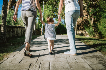 daughter walking hand in hand with her parents in a park