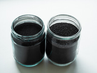 Activated carbon powder for cosmetic face mask in two glass jars, side view on white back