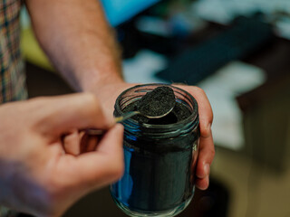 Homemade face mask and scrub with activated powder in glass jar on white back, iron spoon with coal