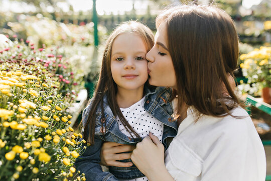 Woman kissing daughter in park. Attractive lady spending time with kid.