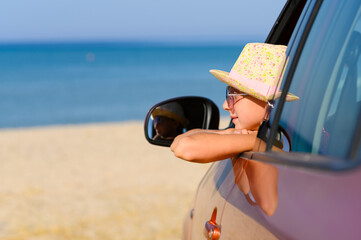 The girl dreamily looks at the sea from the car window. Car travel concept at sea.