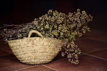 Fototapeta na wymiar There is dried oregano in a small wicker basket against a dark background on brown tiles