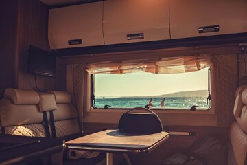 Campervan caravan vehicle for van life holiday on mobile home camper mobile motor home. Serene morning in campervan. Sun is painting everything around in golden. Blue water reflects powerful sunshine
