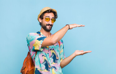 young bearded tourist man smiling, feeling happy, positive and satisfied, holding or showing object...