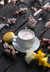 Obraz na płótnie Canvas Cup of hot coffee with macaroon cookies and spring flowers on the old rustic black wooden tabletop.