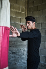 A handsome man in a black shirt punching a boxing bag