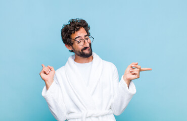 young bearded man wearing a bath robe smiling, feeling carefree, relaxed and happy, dancing and...