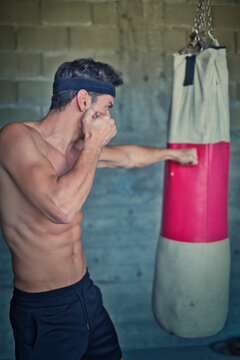 A handsome young man practicing boxing on a punching bag