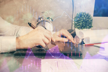 Double exposure of man's hands holding and using a phone and financial graph drawing. Analysis...