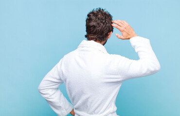 young bearded man wearing a bath robe thinking or doubting, scratching head, feeling puzzled and...