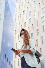 Working woman looking at camera with a smartphone in her hand. He wears a mask for the coronavirus pandemic.