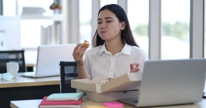 Businesswoman sitting on the chair eating pizza for lunch while working