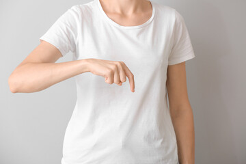 Young deaf mute woman using sign language on grey background