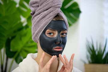 Young woman applying black mud face mask on her face.