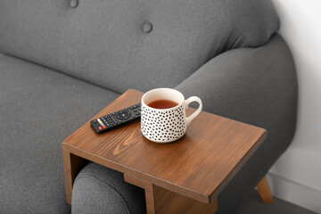 Cup of tea with remote control on armrest table in room
