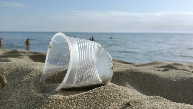 Disposable plastic glass discarded on sandy sea coast ecosystem,nature pollution