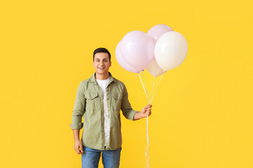 Young man with balloons on color background