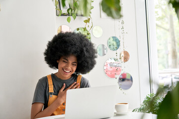 Happy hipster African American female student with Afro hair using laptop computer laughing sitting...