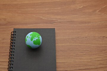 A notebook and a ball of earth placed on a wooden board.