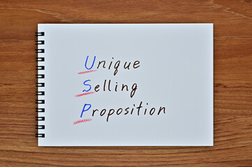 A sketchbook with "Unique, Selling, Proposition" written on it is placed diagonally on a wooden board.