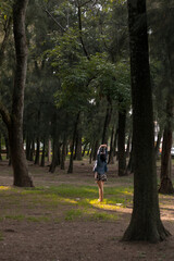 Fototapeta premium Mujer morena joven disfrutando del aire libre en un parque con muchos arboles.