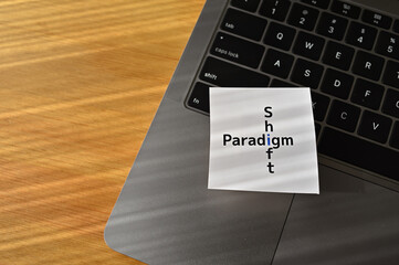 There is a laptop on the desk with the crossword "paradigm" and "shift" on a card placed on it.
