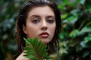 Beautiful young woman with perfect skin and natural make up posing front of plant tropical green...