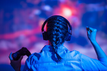 The girl gamer is actively playing games with her back, against the background of a 4k TV, or a...
