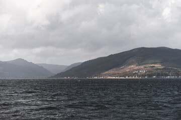 Rocky shore of the Firth of Clyde river, panoramic view from a sailing boat. Dramatic sky after the...