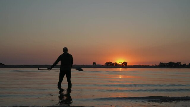 silhouette of a male stand up paddler warming up before paddling workout at sunrise, Boyd Lake State Park popular boating and recreation area in northern Colorado