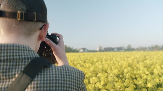 Rear shot of a man taking pictures of yellow blooming rape field in nature during sunny day.German Agriculture.