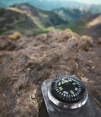 A close up of a compass on a rocky surface pointing north with mountains and valleys in the...
