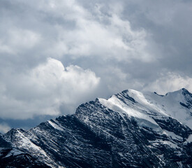 A close up of dramatic snow-capped Swiss Alp mountains in dappled light with moody clouds above in Switzerland