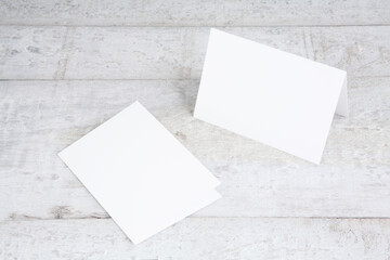 Two white greeting cards mockup on a white wooden desk. Blank, closed card templates. Perspective...