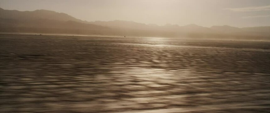 Tiny motorcycle in distance closes toward moving camera on dry lake