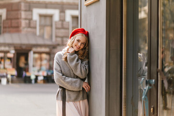 Sweet, shy, romantic European woman is smiling against backdrop of beautiful building. Portrait of girl in red beret.