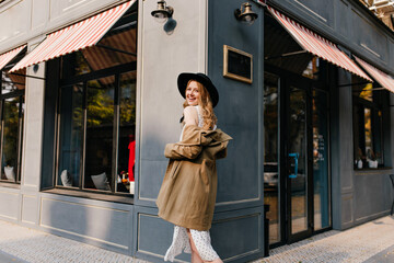 Charming, cute, cheerful, smiling girl walks against a gray building, looking into the camera.