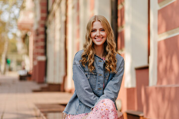 portrait of a smiling blonde girl who is sitting on the street and looking to the camera