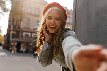 Attractive girl in red hat smiling, looking into the camera, pulling her hand and calling to go...